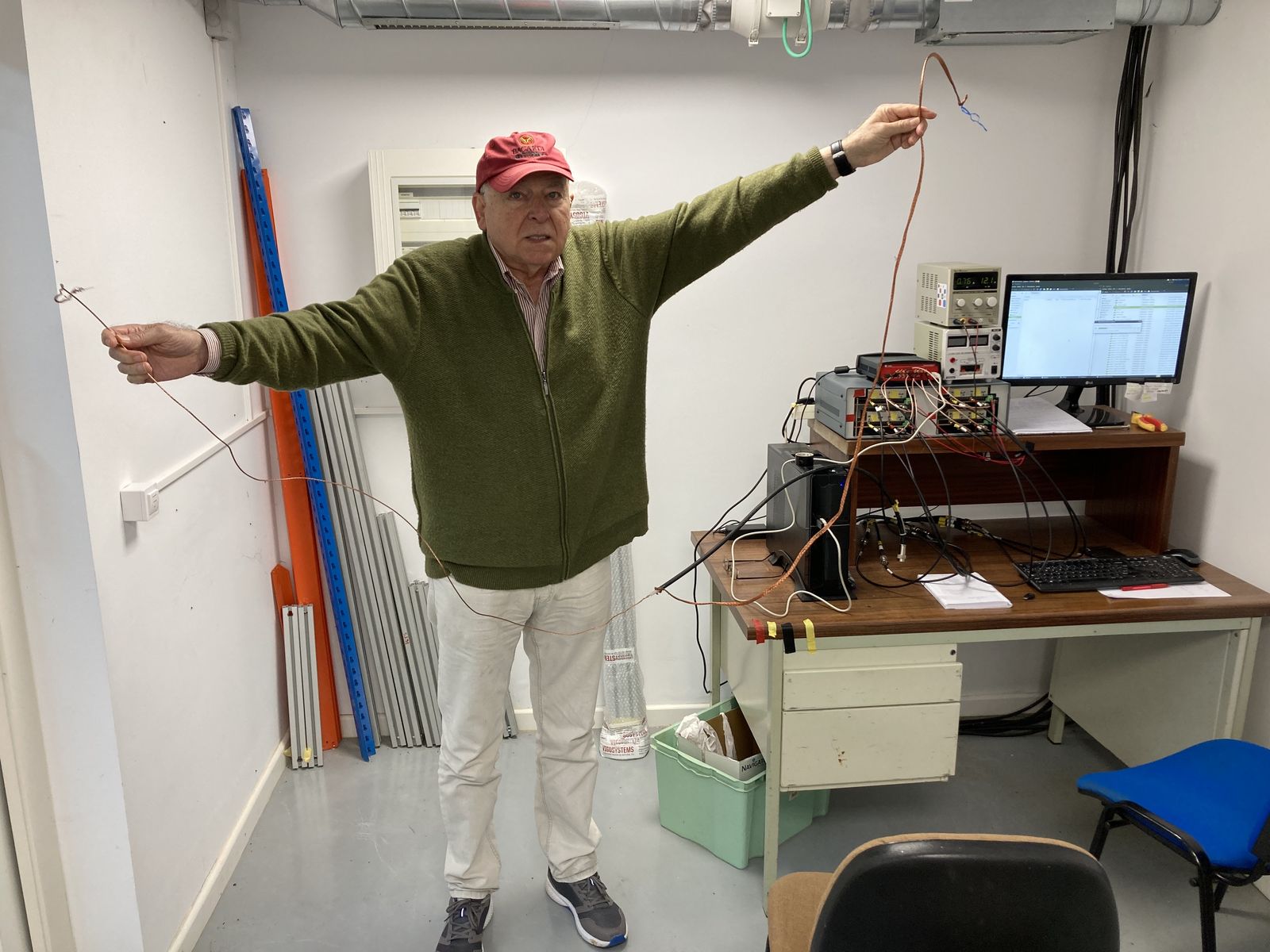 Juan Xuna in a lab, arms outstretched, wearing a red cap